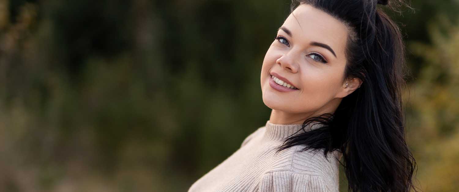 Anika in einem Portrait, seitlich zur Kamera, lächelt sympathisch, trägt ein enganliegendes Kleid, Einladungsbild für die Homepage.