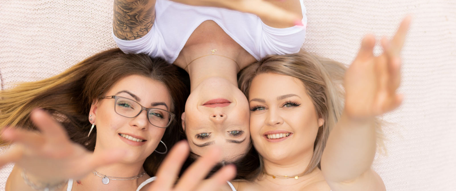 Amelie, Lisa und Romana liegen Kopf an Kopf auf der Decke, alle lächeln zur Kamera und strecken ihre Hände aus, fotografiert in Möringen.