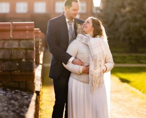 Annabell und Marius stehen an der Burgmauer, Annabell mit einer Jacke, beide schauen sich lächelnd an, während ihrer Winterhochzeit in Tangermünde.