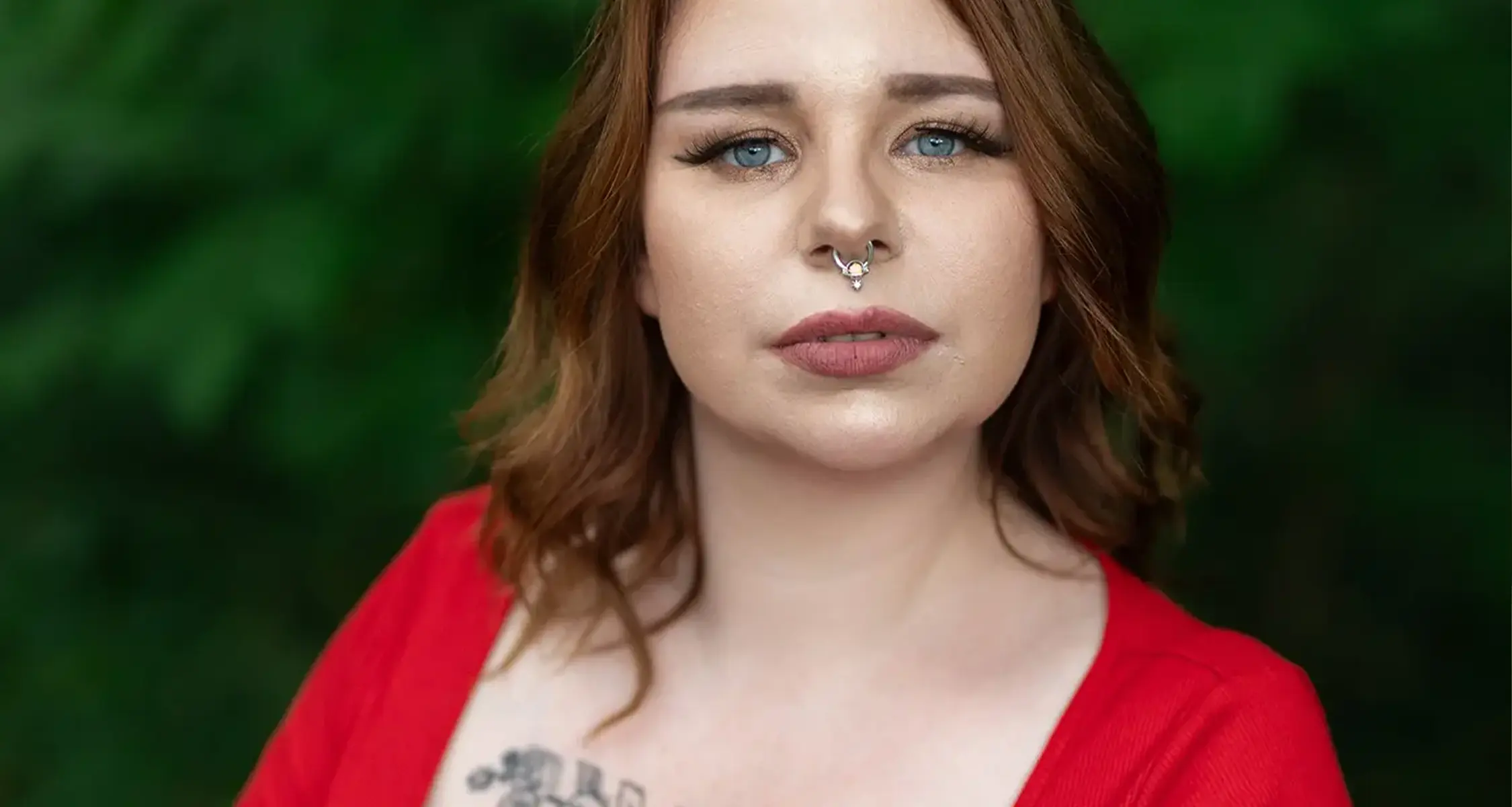 Portrait von Sarah mit intensivem Blick und rotem Oberteil vor grünem Hintergrund